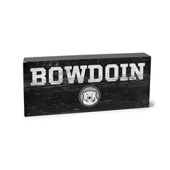 Grey wooden block with distressed imprint of BOWDOIN in white over a black, white and grey mascot medallion.