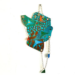 The artwork 'Climb the Blue' by Sunny Chapman features an abstract geometric collage in vibrant turquoise and copper tones. Mosaic-like patterns and textures created with acrylic painted papers shimmer with glitter accents. Metal chains, grommets, and decorative plastic jewels add dimensional elements, while handcrafted charms dangle beneath the main composition.