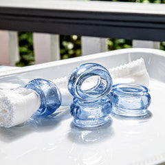 Four Provence Napkin Rings by Juliska are displayed on a white tray, one holding a folded white napkin. Set outdoors with greenery, the rings add vibrant color and style to the table. Sold as a set of 4.
