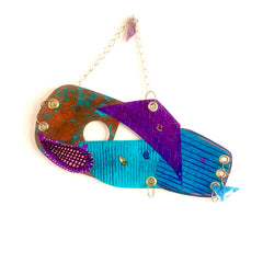 The artwork 'Swinging' features an abstract composition with vibrant turquoise, purple, and rust-colored geometric shapes arranged in a flowing design. The acrylic on paper piece showcases textured patterns including dotted details and linear striations, suspended by a delicate gold chain. 16x18 inches artwork by Sunny Chapman.