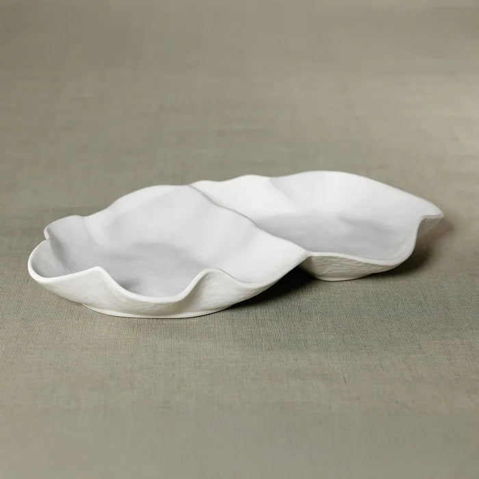 The Alto Two Section Ceramic Serving Bowl by Zodax, featuring a matte white petal-like design with wavy edges, rests on a muted green textured surface.