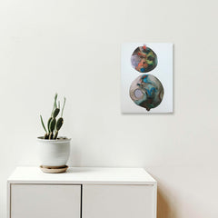 The artwork 'c2' by Arielle Stein features two circular forms in fluid watercolor and acrylic ink. The top circle displays swirling oranges and deep purples, while the larger bottom circle showcases flowing turquoise and earth tones creating a mesmerizing marble-like effect against a white paper background. The abstract composition evokes planetary or celestial imagery. By Arielle Stein.