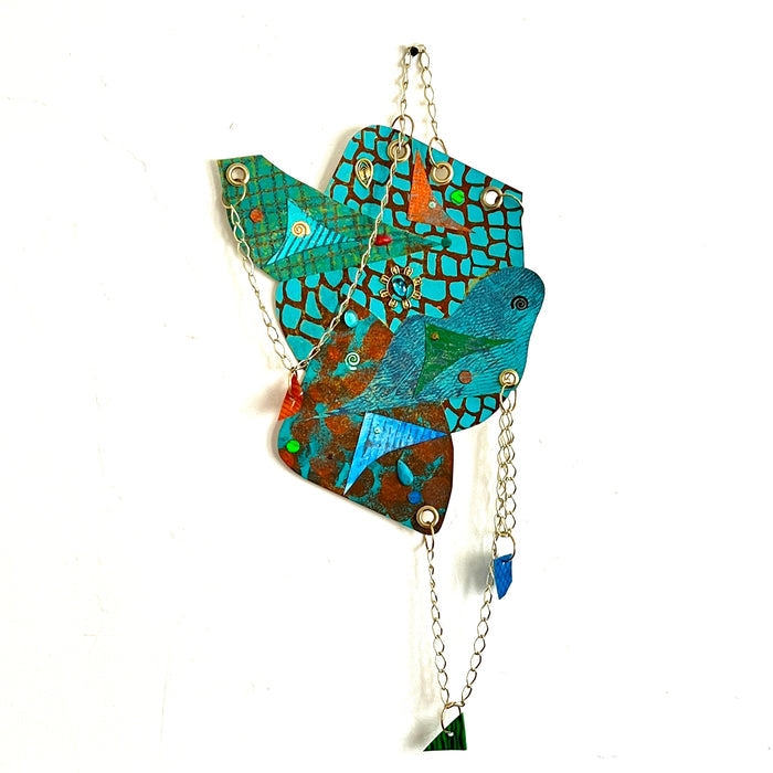 The artwork 'Climb the Blue' by Sunny Chapman features an abstract geometric collage in vibrant turquoise and copper tones. Mosaic-like patterns and textures created with acrylic painted papers shimmer with glitter accents. Metal chains, grommets, and decorative plastic jewels add dimensional elements, while handcrafted charms dangle beneath the main composition.