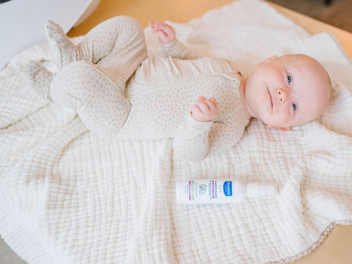 Mustela USA | Diaper Rash Sprayable Cream next to baby on a bed