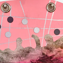 The artwork 'Juggler' by Sunny Chapman features an abstract composition on pink paper with intersecting silver lines creating a grid pattern. Black and metallic circular elements float above a textured brown-grey form, suggesting movement and balance. Metal grommets anchor the top corners of this mixed media piece combining monotype prints and marker details.