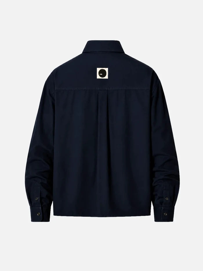 shopi go Meguro Regular Shirt – Navy, arka görünümde orta üstte beyaz kare rozet ve siyah daire