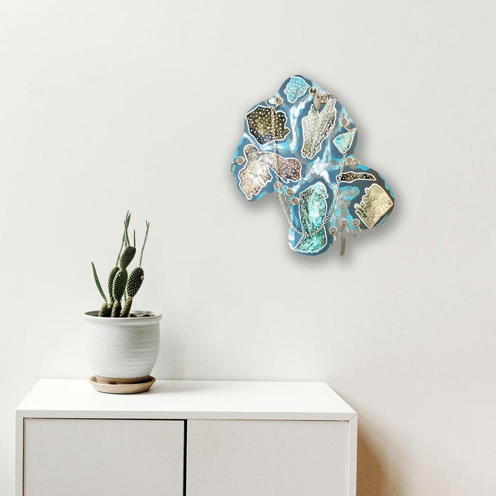 The artwork 'Noumenon' by Sunny Chapman features abstract crystalline formations in shades of aqua blue and metallic silver, resembling fractured geodes or ice formations. The acrylic painting on paper creates a striking dimensional effect with intricate patterns and textural elements against a stark white background. 16x12 inches acrylic artwork by Sunny Chapman.