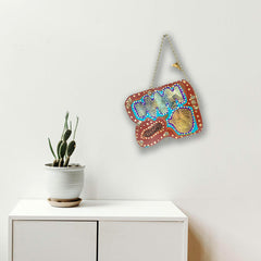 The artwork 'Remembrance 6' by Sunny Chapman features an abstract composition in rich terracotta red with vibrant turquoise blue accents and metallic gold elements. The piece showcases organic shapes with dotted border details, creating a harmonious flow across the 12x14 inch acrylic on paper surface. Hung by a delicate chain against a white wall near a potted cactus.
