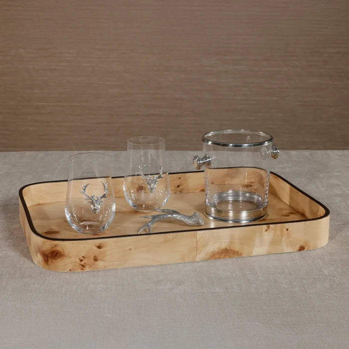 The Zodax Valari Rectangle Serving Tray in light burl veneer holds two stemless glasses with silver deer accents, a clear ice bucket with a silver lid, and a deer antler-shaped silver bottle opener on a beige surface.